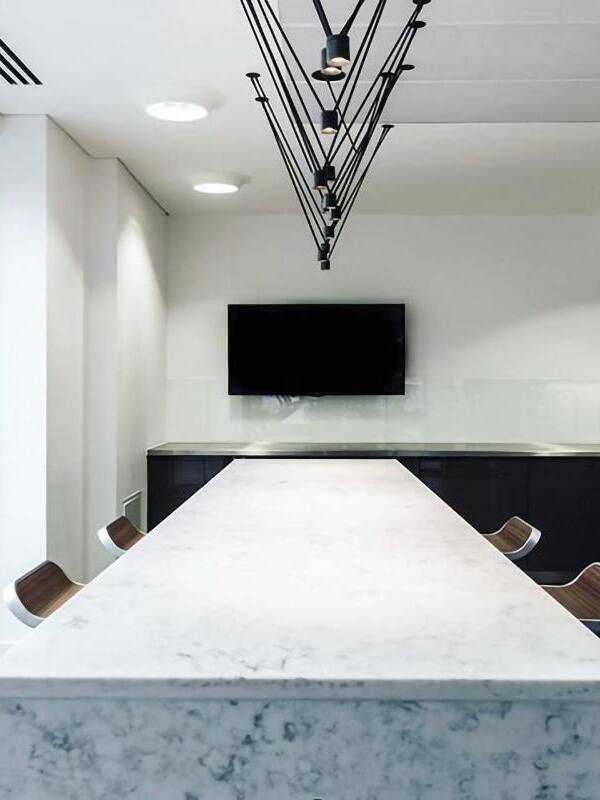 Black cylindrical pendant heads aligned over a pale marble-like table facing a wall television