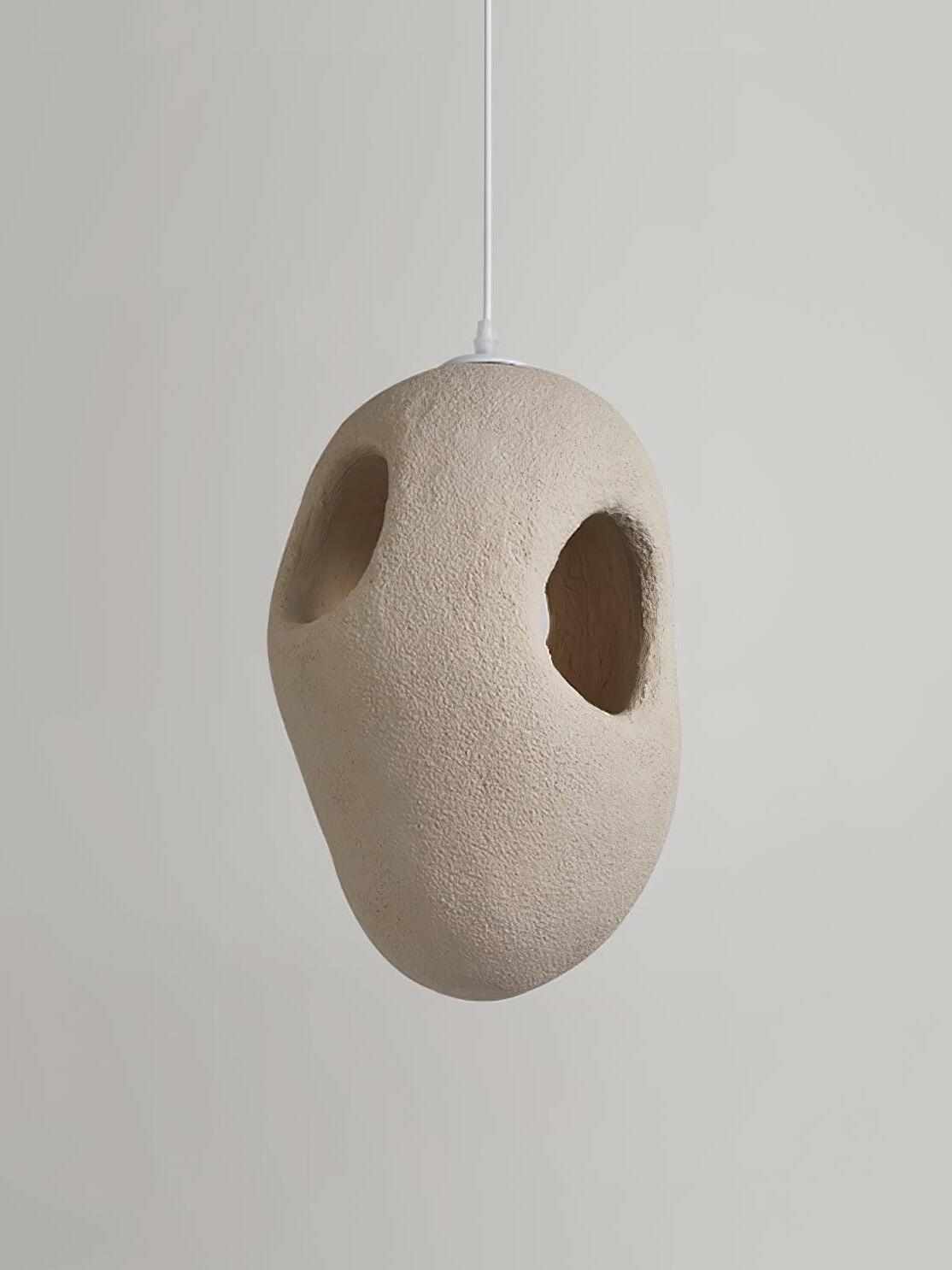 Unlit cream-looking rounder pendant with two smaller openings, rough texture and a White cord against Gray