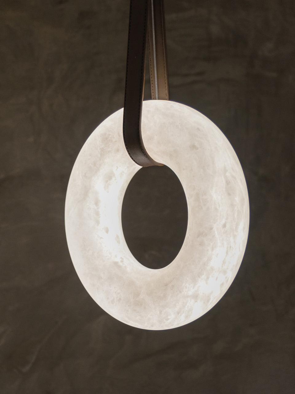 Upright white alabaster ring held by a dark brown strap