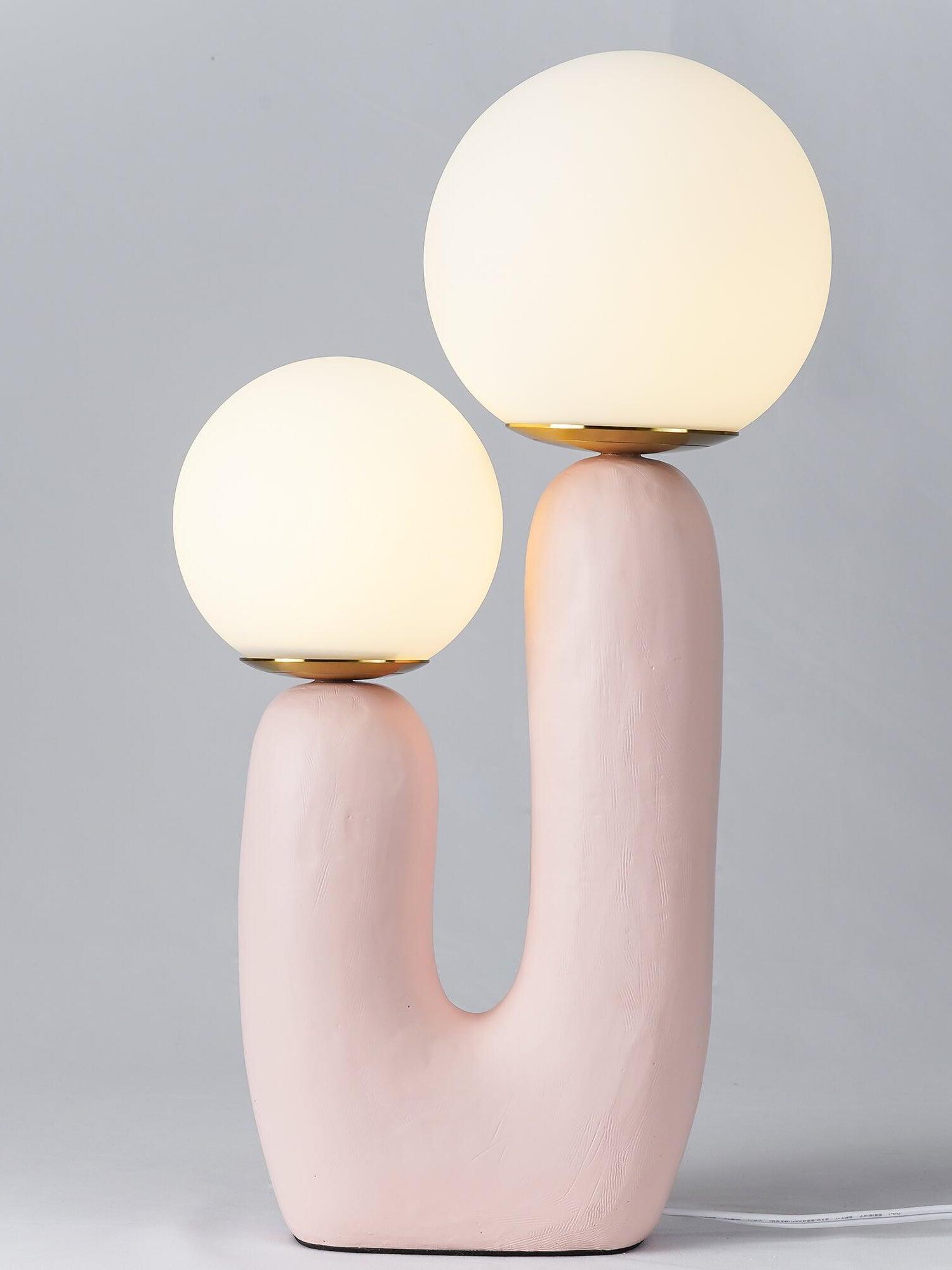 Pink Oo Rough lamp close view with glowing globes above textured U-shaped body, warm-metal collars and cord right