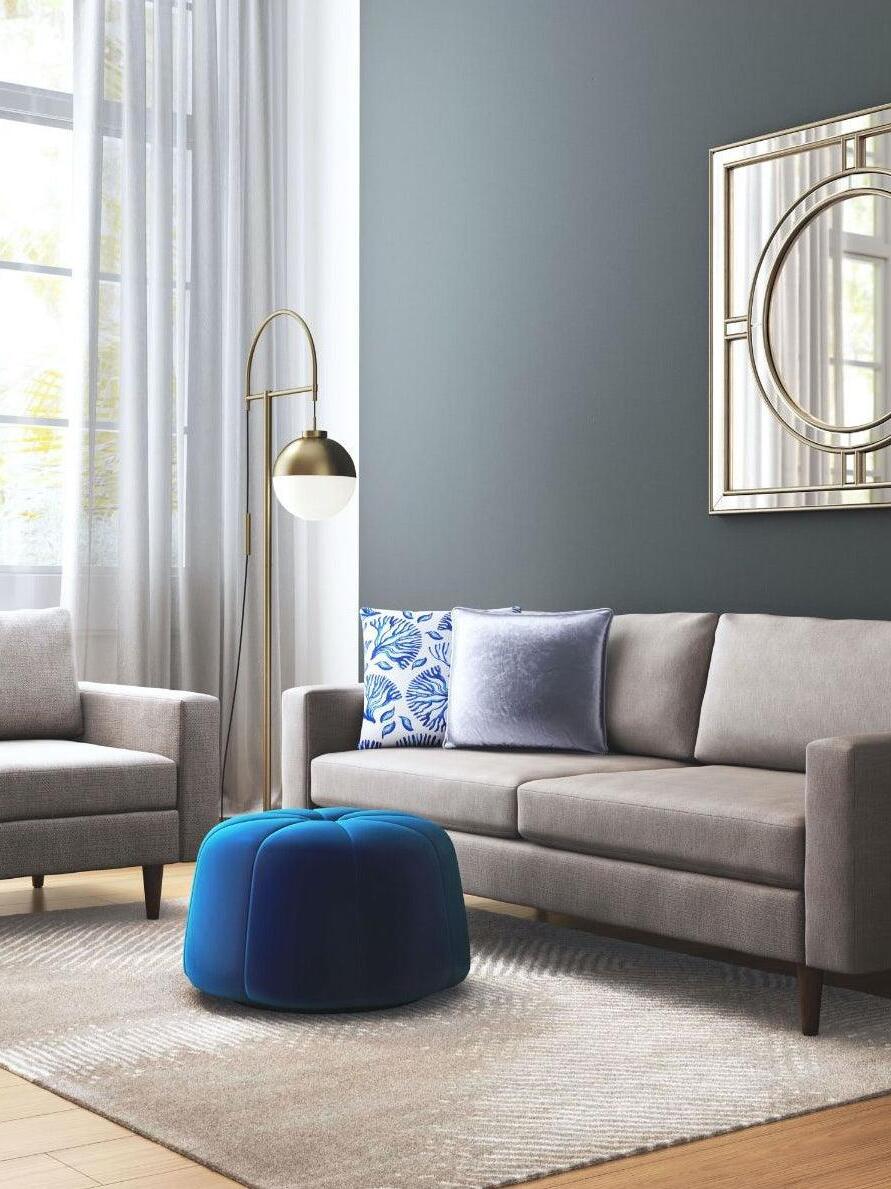 Waterloo Gold floor lamp beside a sofa and blue ottoman