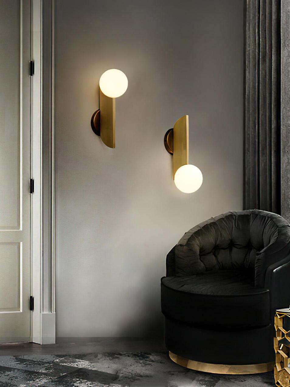Two lit globe wall lamps at staggered heights beside a dark chair, one globe up and one down