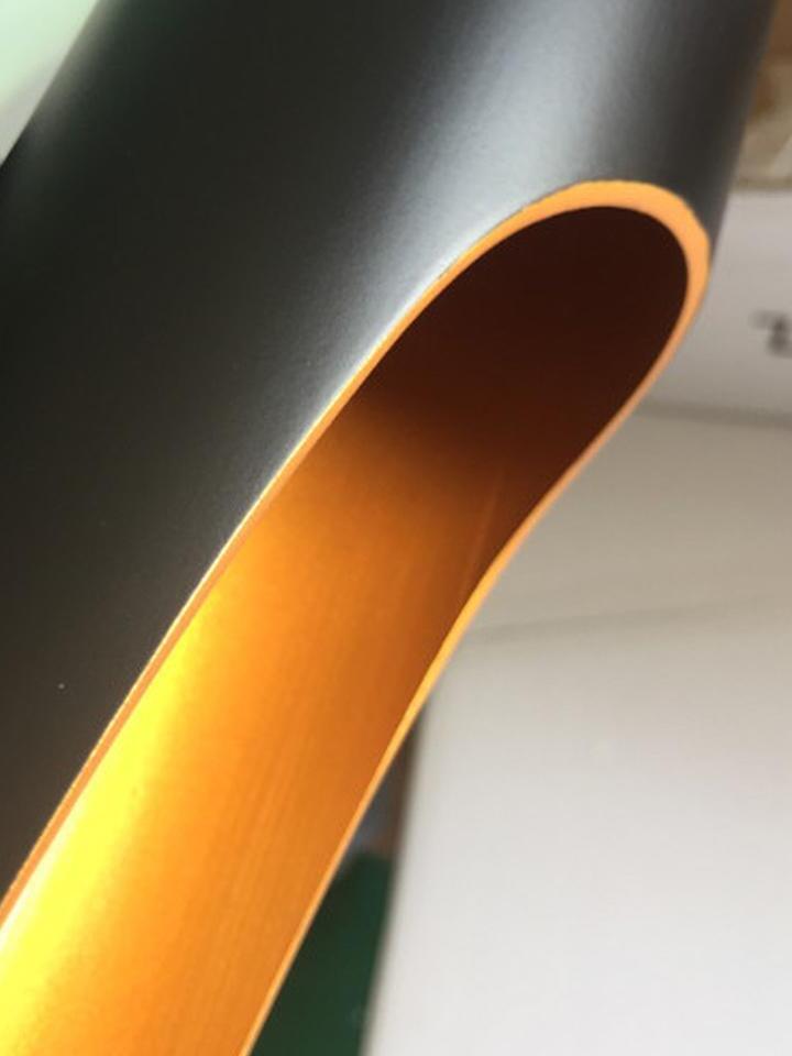 Close-up of a diagonal pipe opening with a gold-tone interior and matte black outer surface