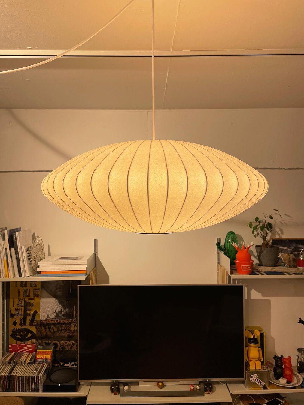 Warmly glowing flattened oval ribbed pendant above a television and shelving