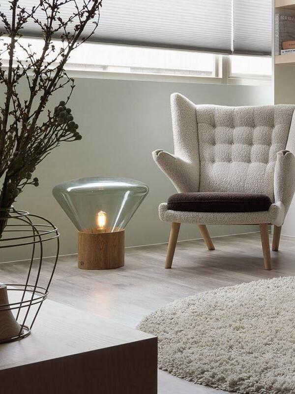 Flared glass lamp at floor level beside upholstered wing chair and window