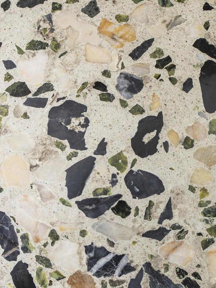 Close terrazzo surface with dark, green and beige chips in pale matrix