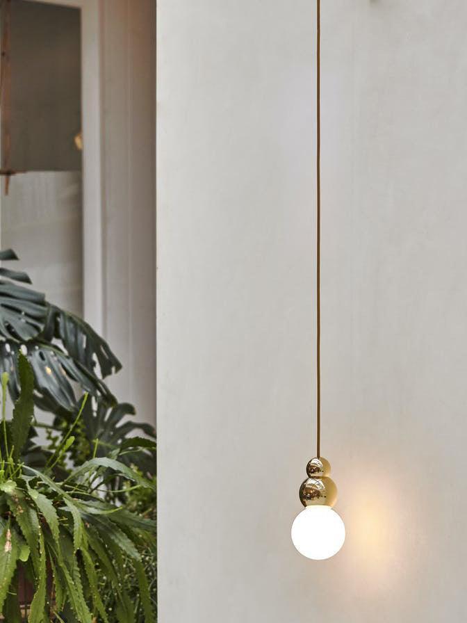 Gold hanging ball light against pale wall near leafy plants