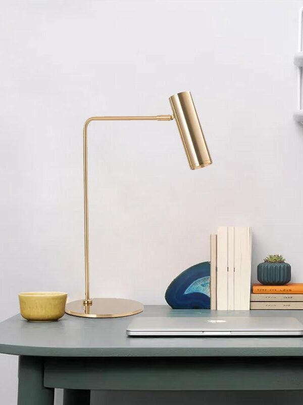 Gold-tone bent-arm lamp with angled head beside books and desk decor