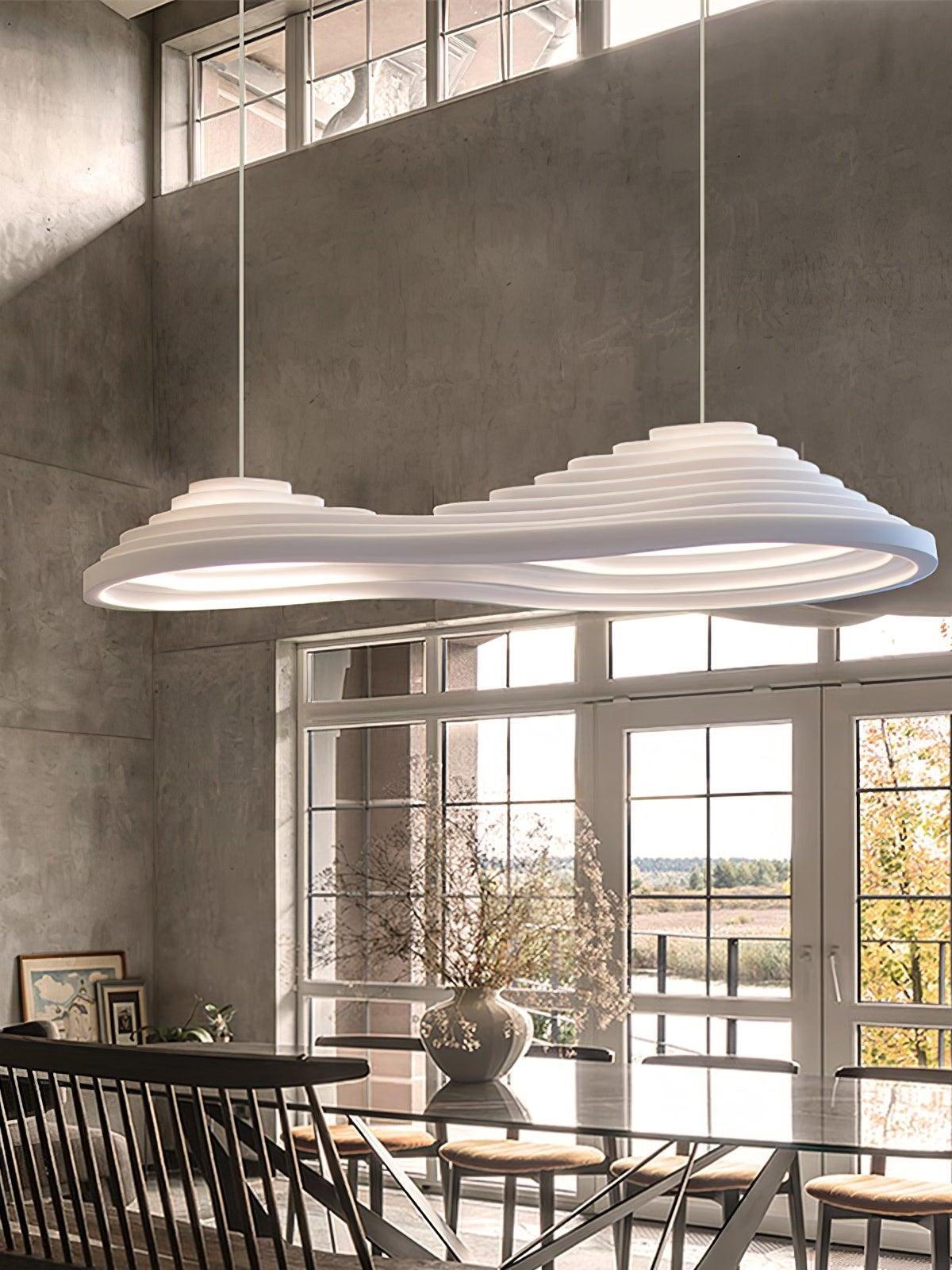 Elongated white pendant with two raised contours above a table near tall industrial windows.