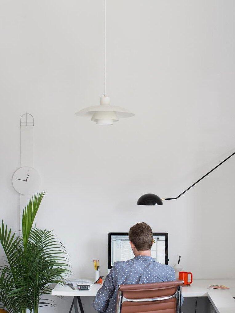 Black dome wall lamp over a person at a computer desk, with a separate white layered ceiling pendant above