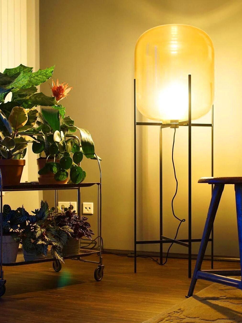Bright amber lamp on a tall black frame in a warmly lit corner.
