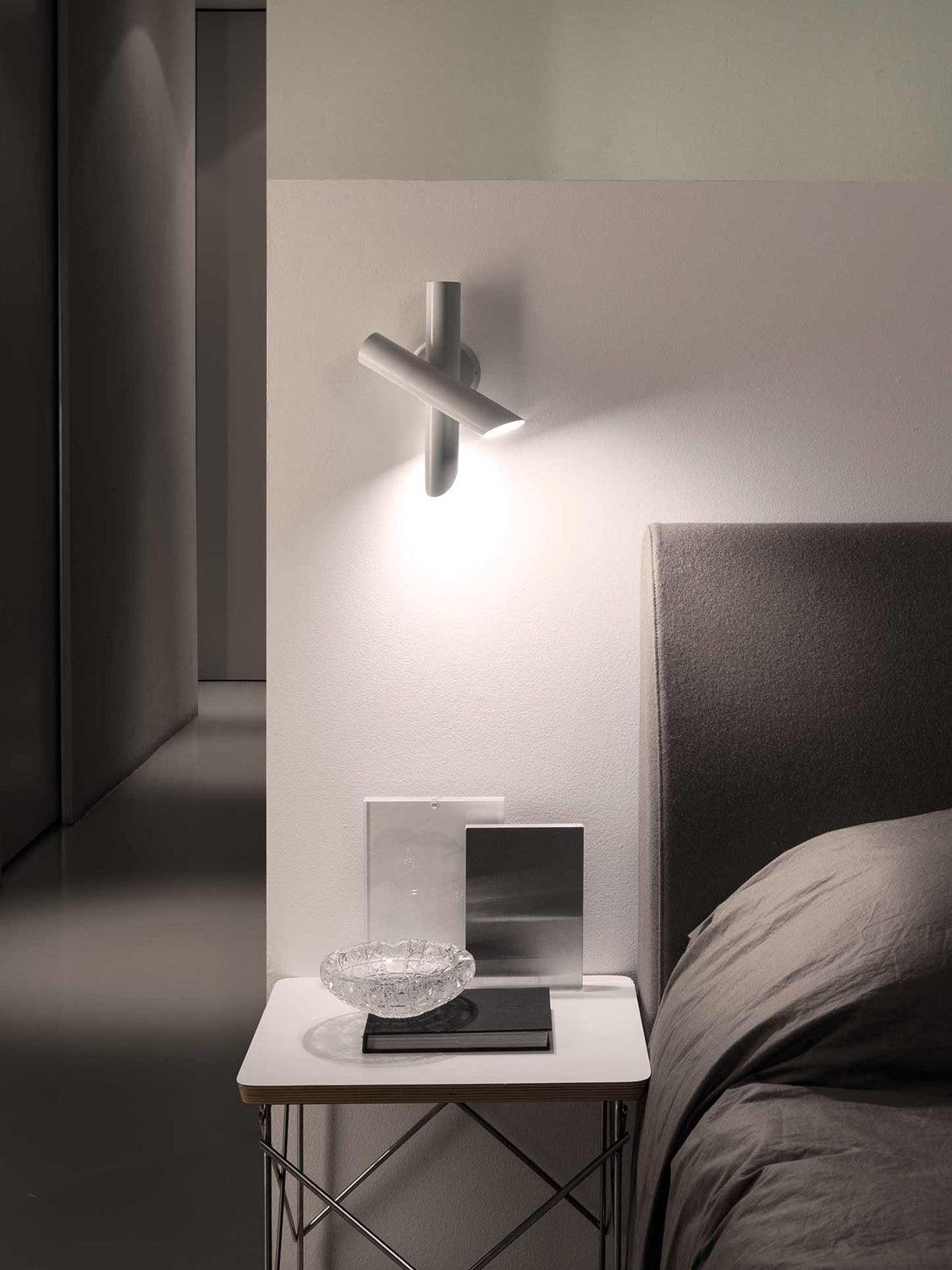 White crossed-tube lamp above bedside table