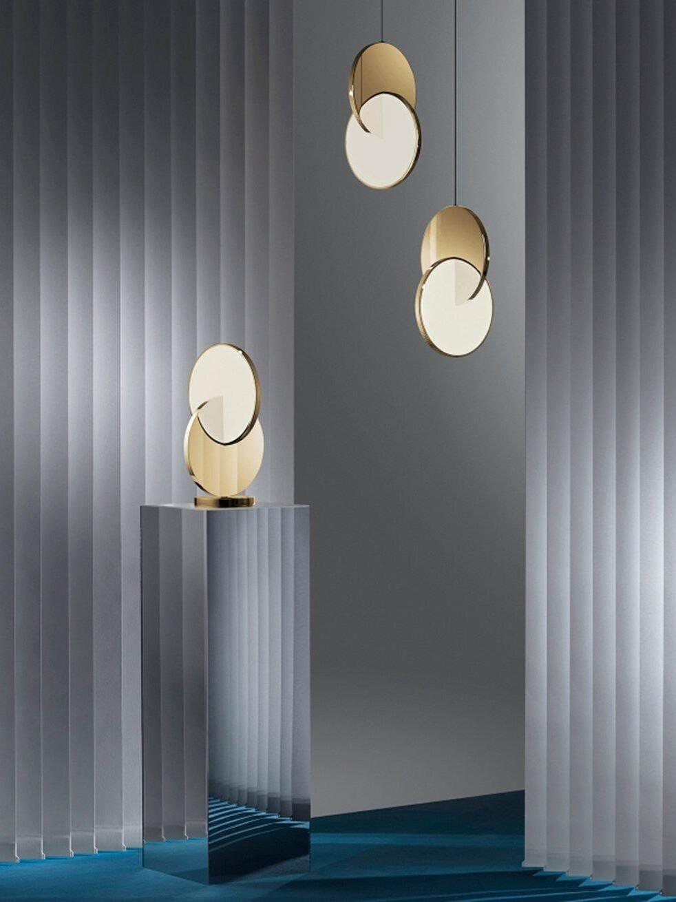Two gold disc pendants beside a separate table lamp on a mirrored plinth and white room dividers