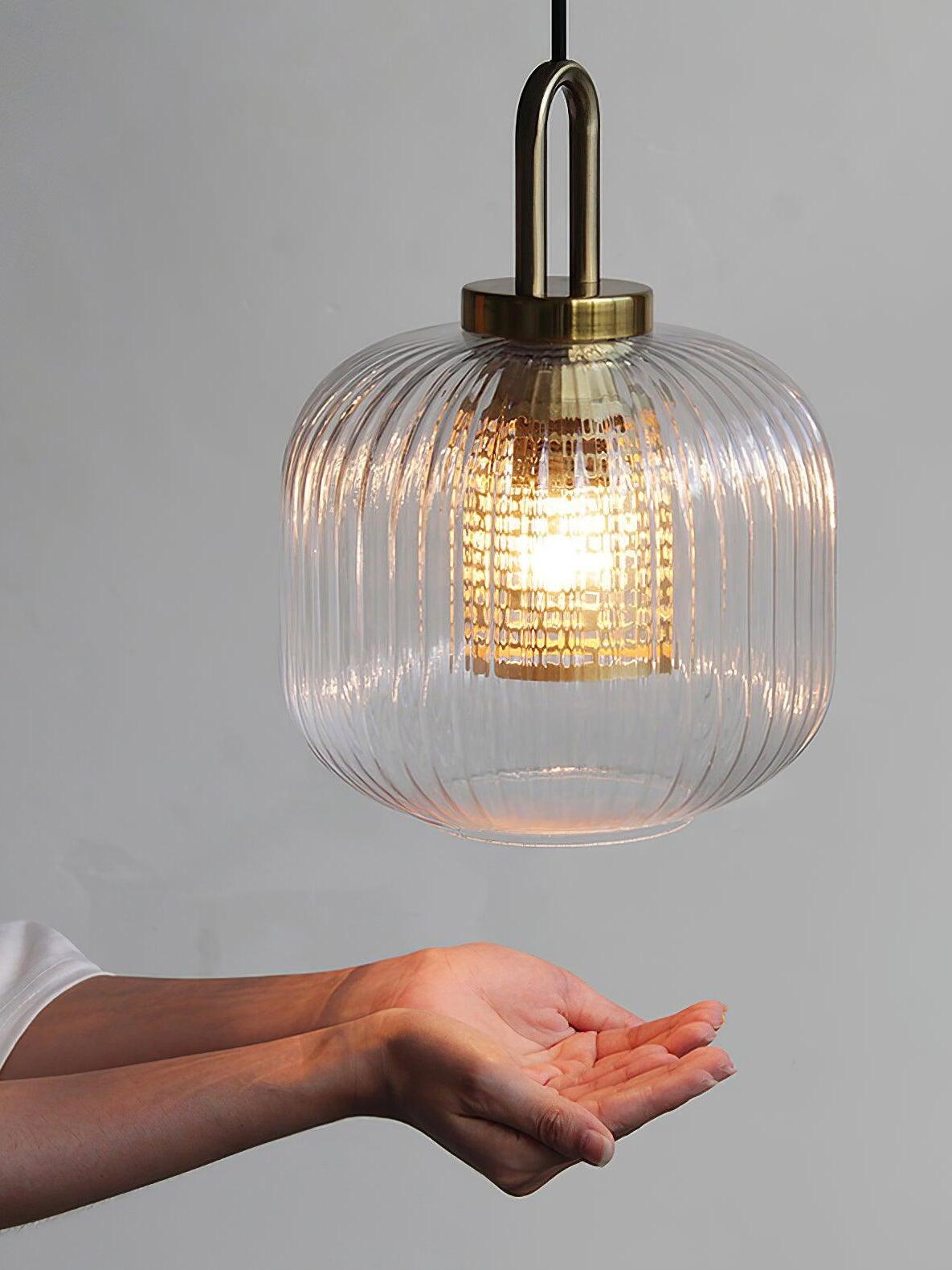 Hand beneath a clear ribbed-glass pendant