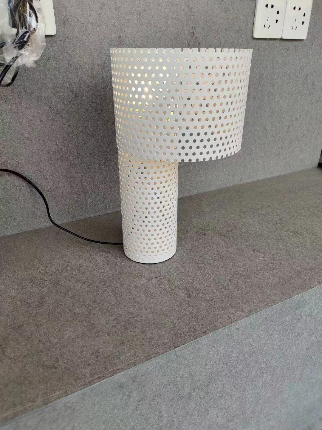 White perforated metal lamp on grey surface near outlets