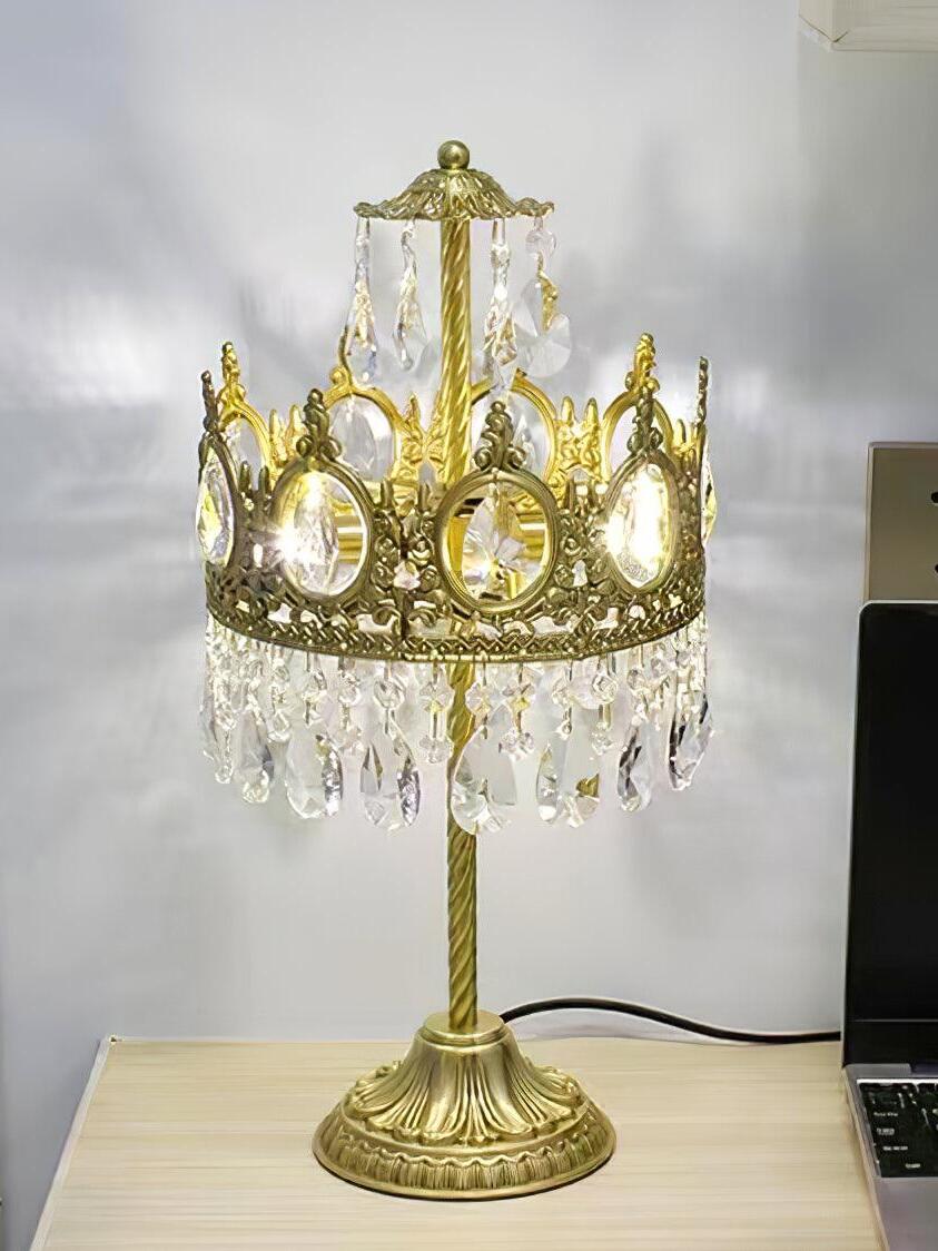 Unlit crystal table lamp with upper drops on a light wooden surface against a grey wall.