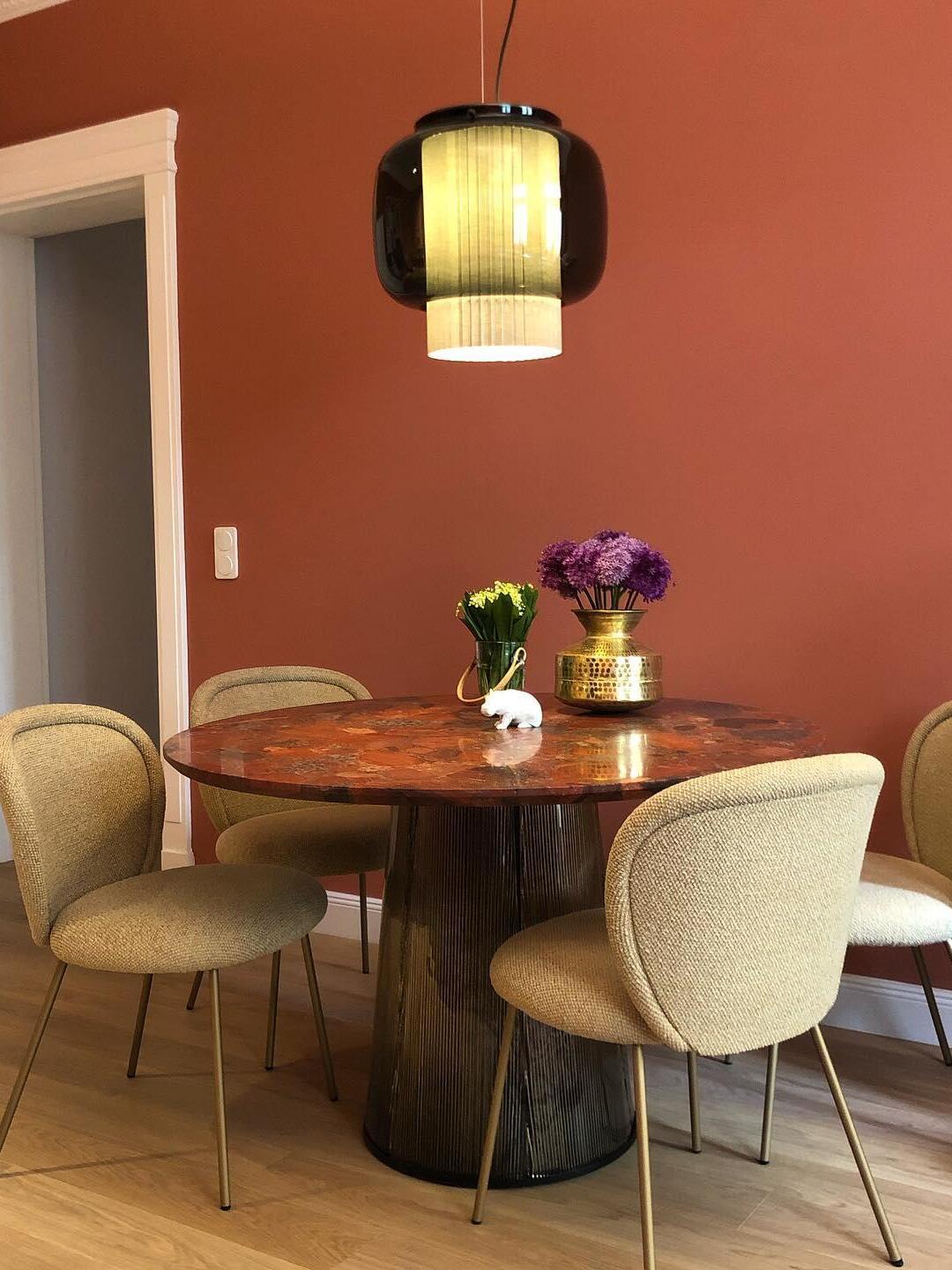 Black and smoke-grey Manila T pendant light above a round reddish dining table with pale chairs and flower vases