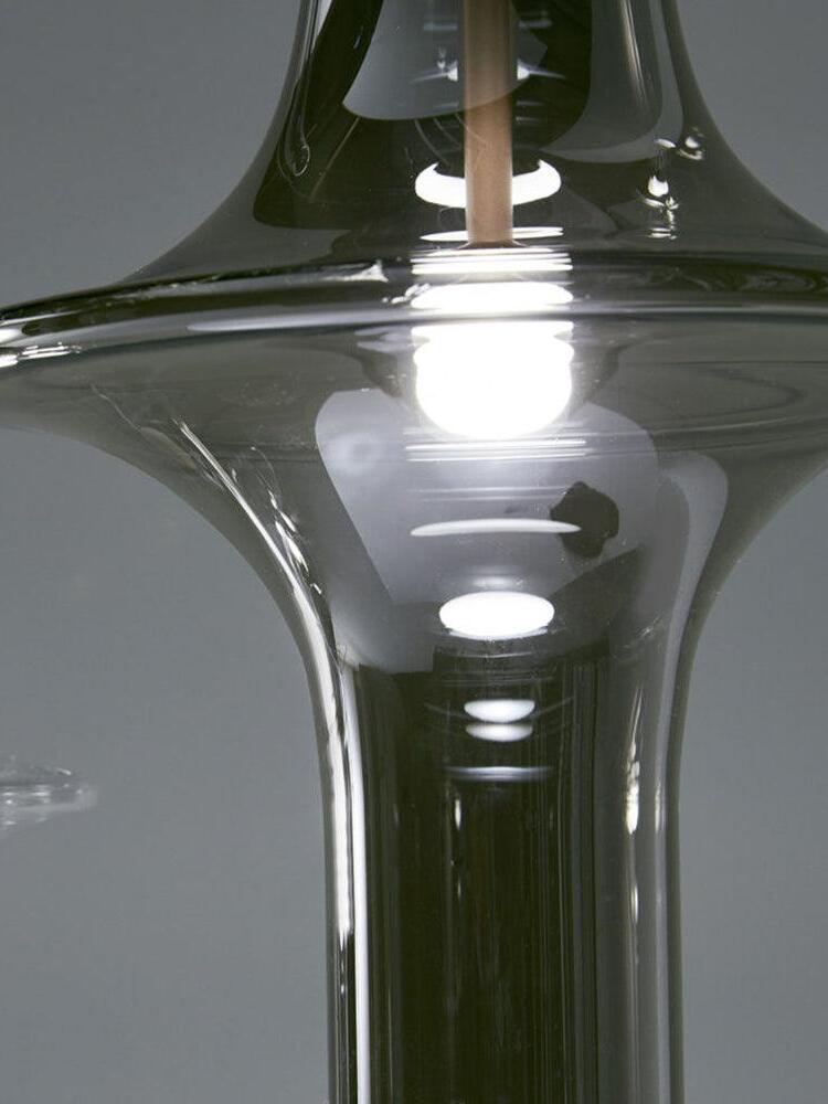 Bright light point inside a smoky flared glass shade, with gold-tone stem and reflections in the lower tube