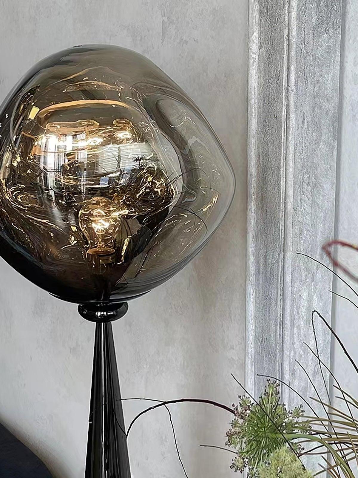 Close view of a smoky globe shade and black cone base beside flowers and a pale curtain