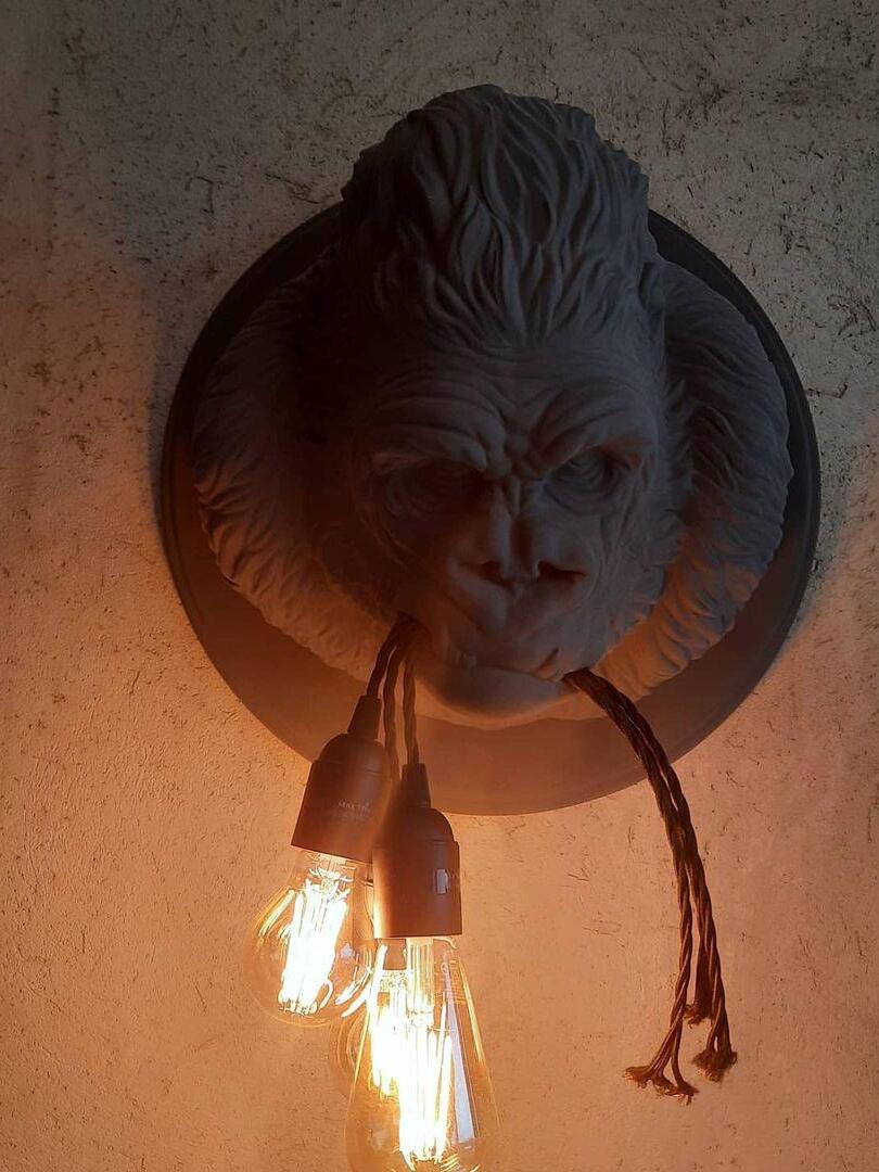 Dark sculpted gorilla head with glowing elongated bulbs against textured wall