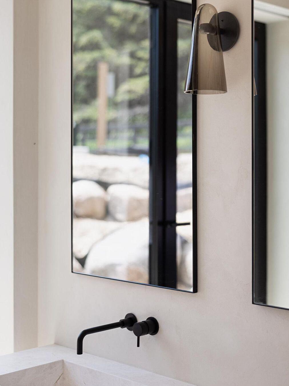 Dark glass wall fixture beside a mirror and window