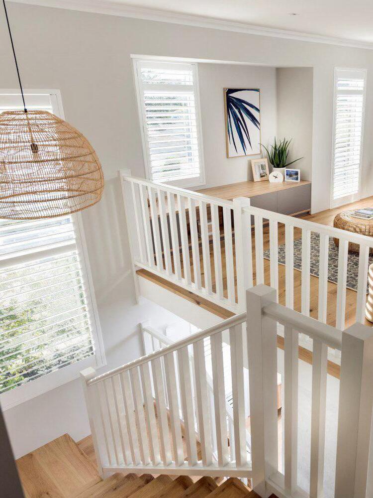 Natural wicker pendant beside white stair railings and windows