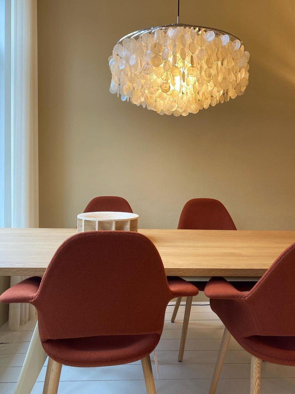 Round shell chandelier above a table with red chairs