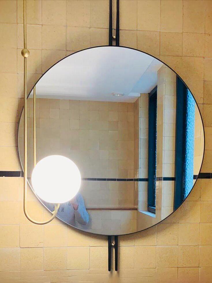 Single curved-arm globe pendant beside a round mirror