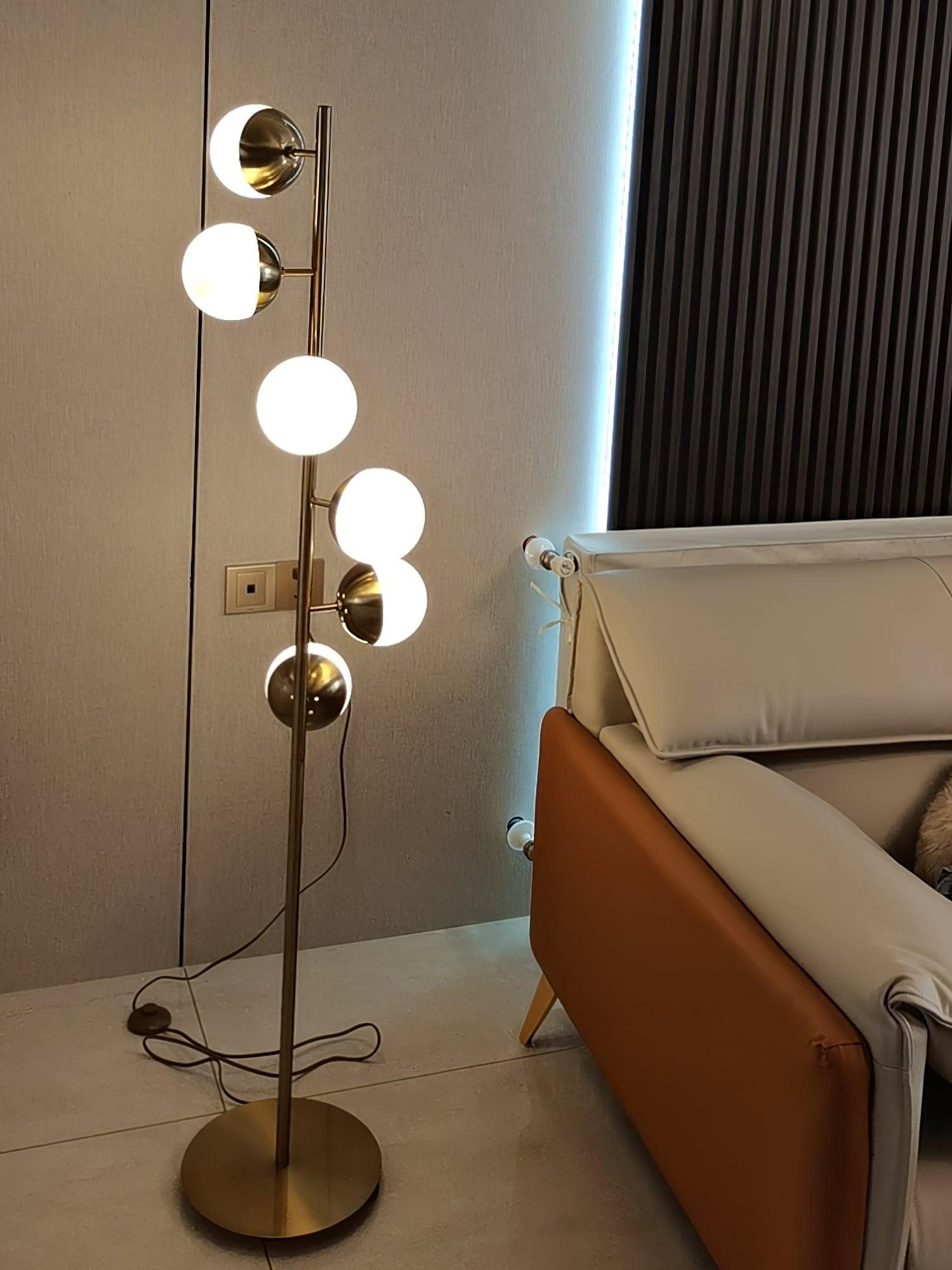 Tall gold lamp beside tan sofa with cord visible