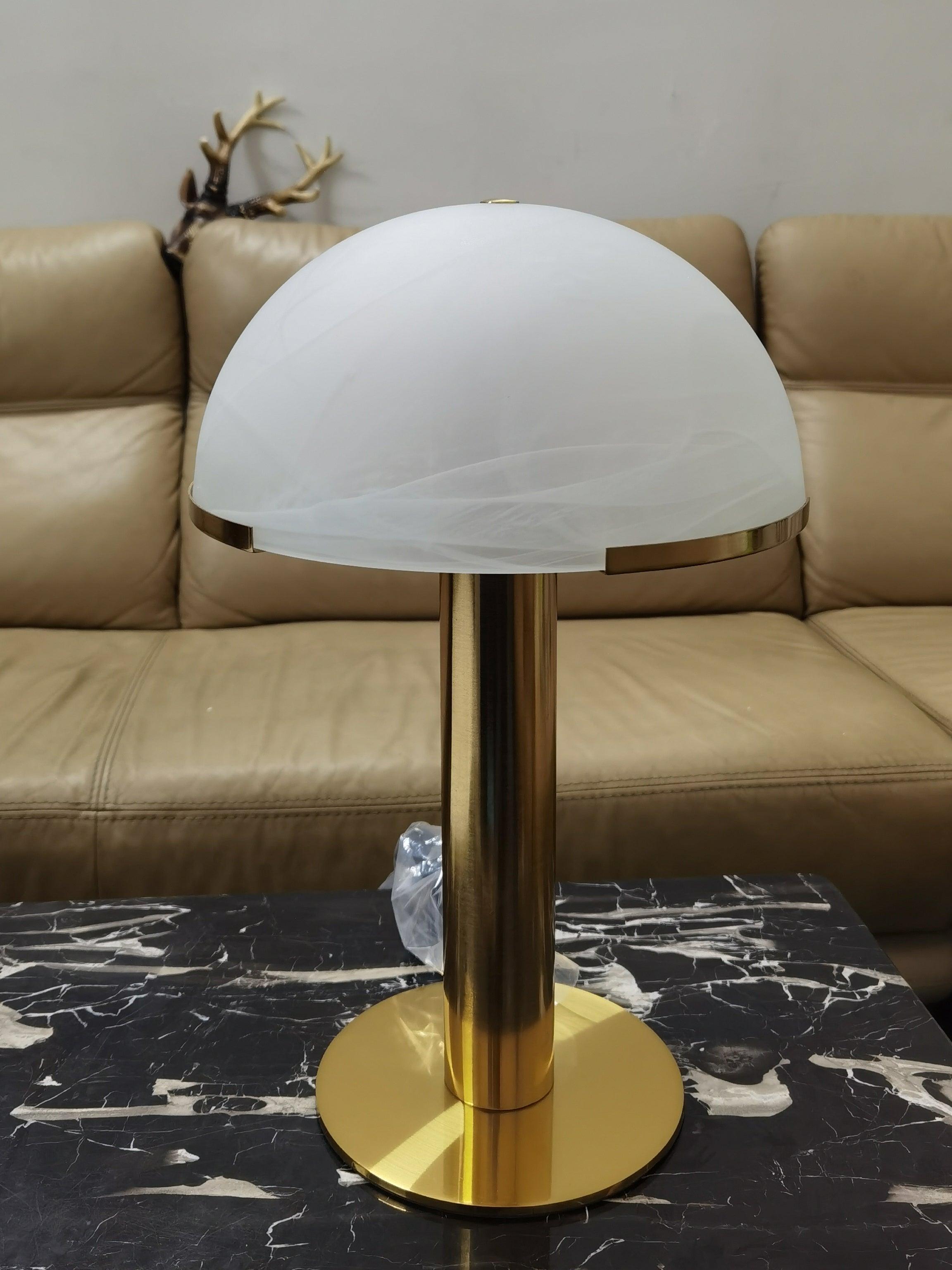 Pale dome with faint diagonal veining above a gold-coloured stem on a dark marble-patterned table