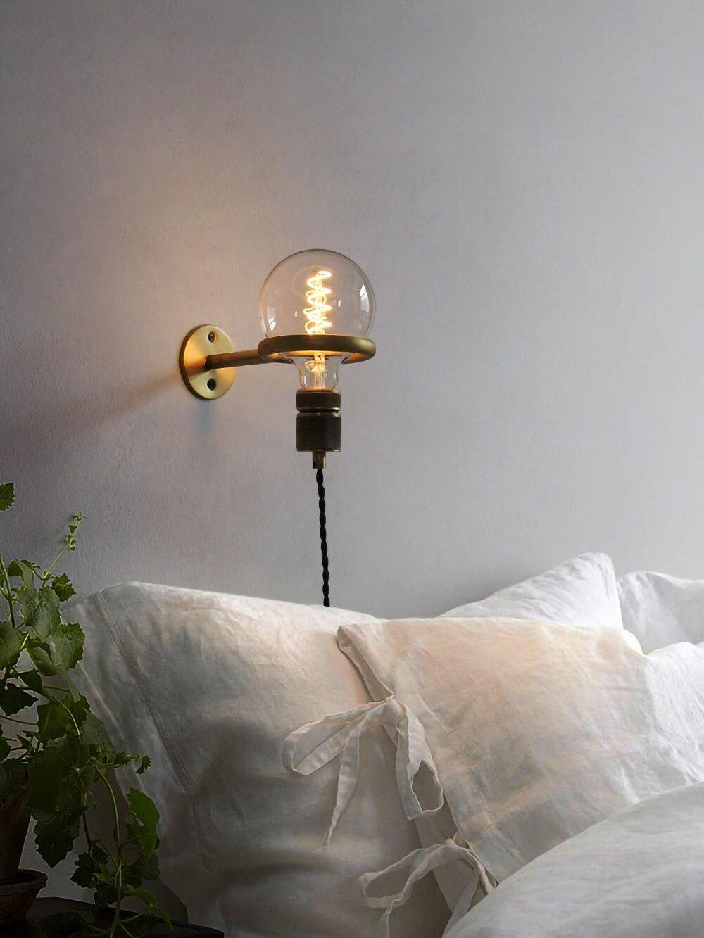 Lit globe loop wall light above bed and cushions