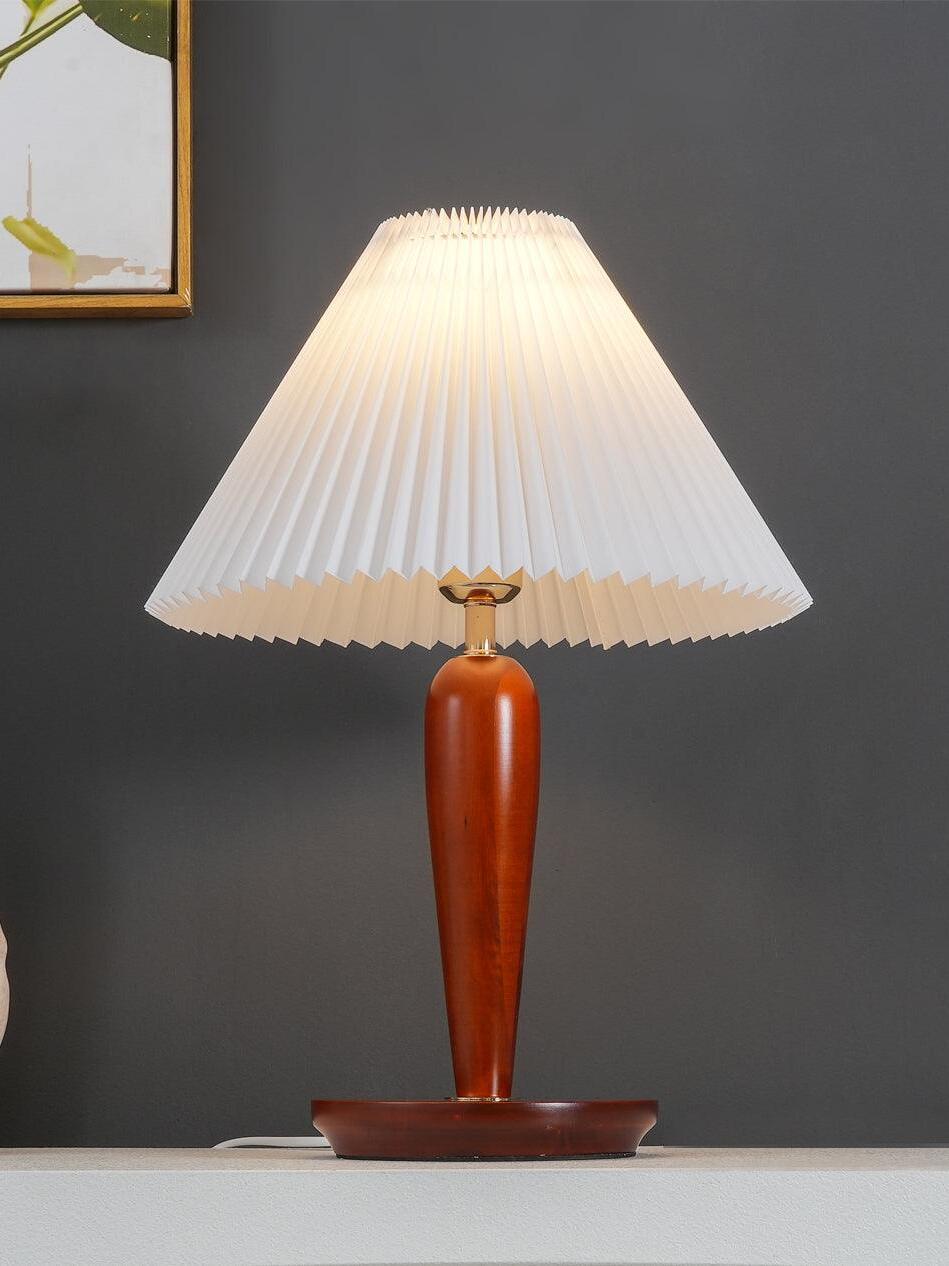Lit brown table lamp with pleated shade against dark wall