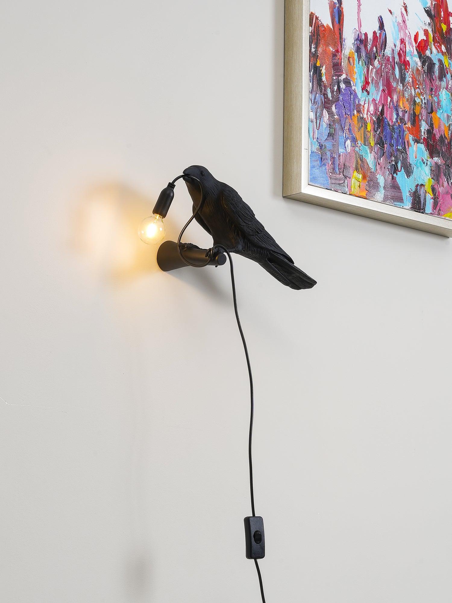 Black bird facing left beneath artwork, holding a lit bulb cord above an inline switch