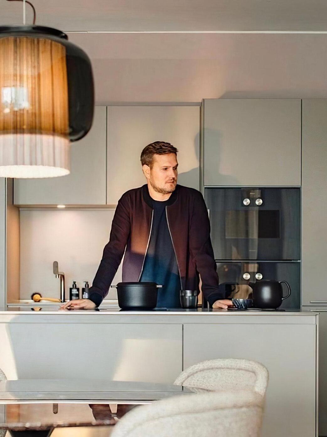 Kitchen scene with part of a Manila T pendant at upper left, a person at the counter and pale grey cabinets