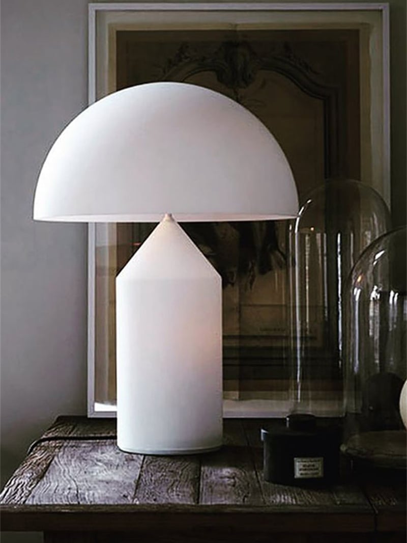 White mushroom table lamp on a rustic wooden cabinet before framed artwork and glass display domes