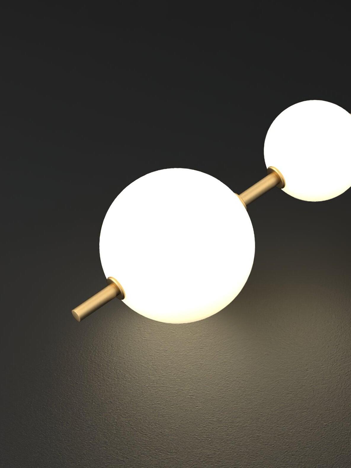 Close-up of two glowing white globes, brass-tone joining stem and lower tail against dark gray