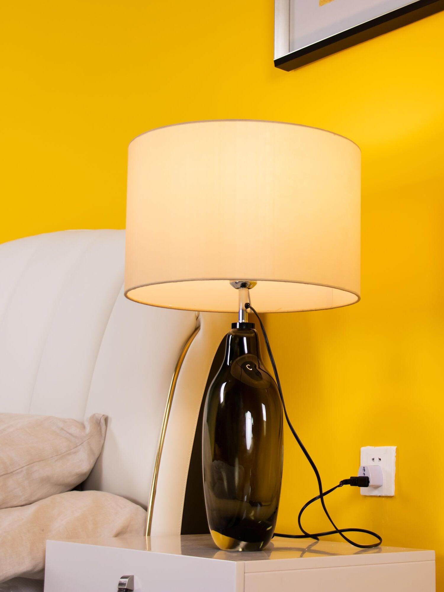 Illuminated drum-shade lamp beside sofa against yellow wall