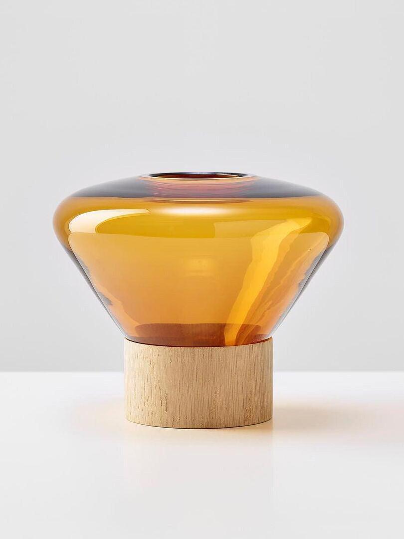 Isolated broad amber-yellow rounded glass shade with top opening on pale wood base