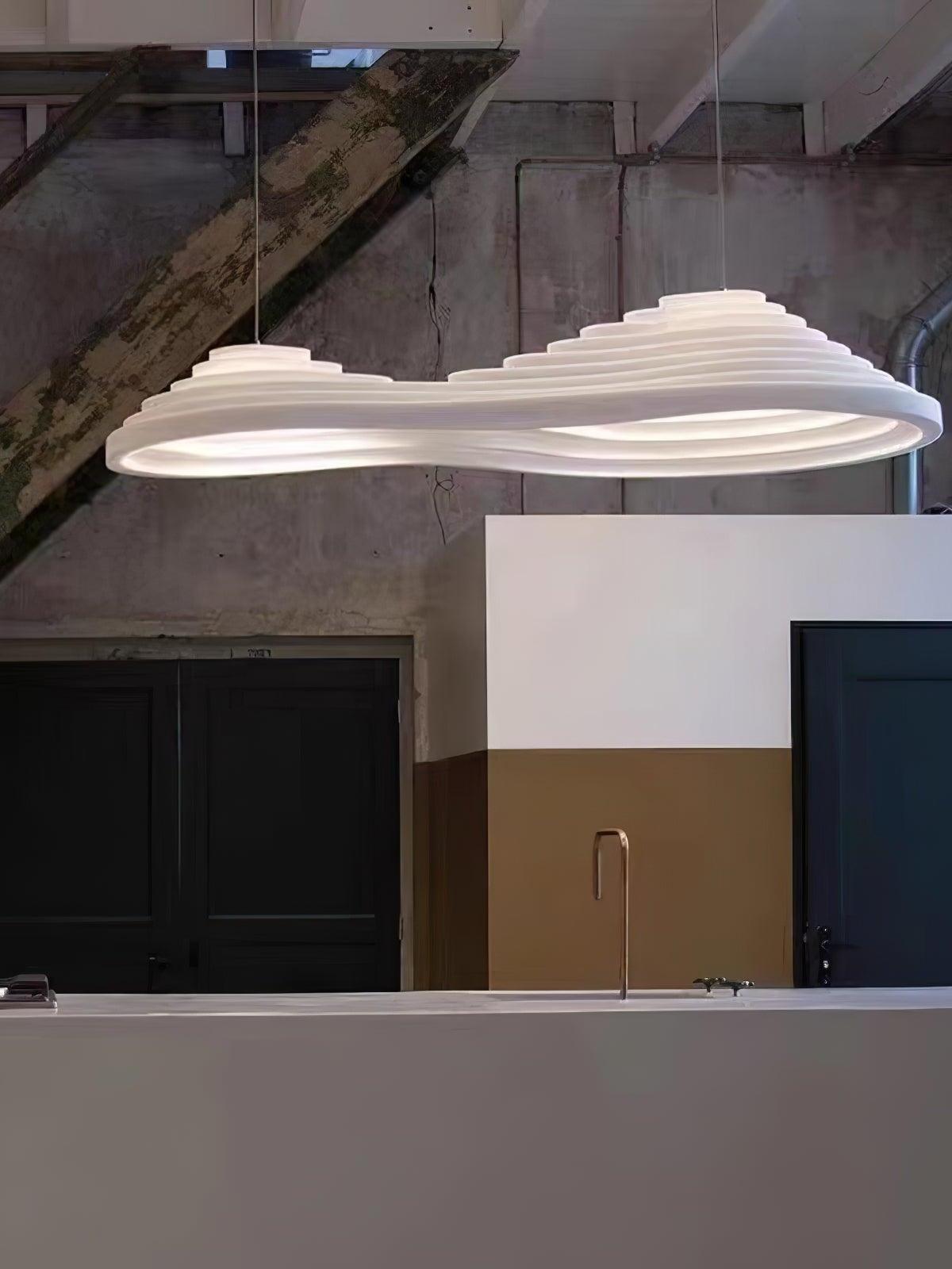 Elongated white pendant with two raised sections over a counter in an industrial interior.