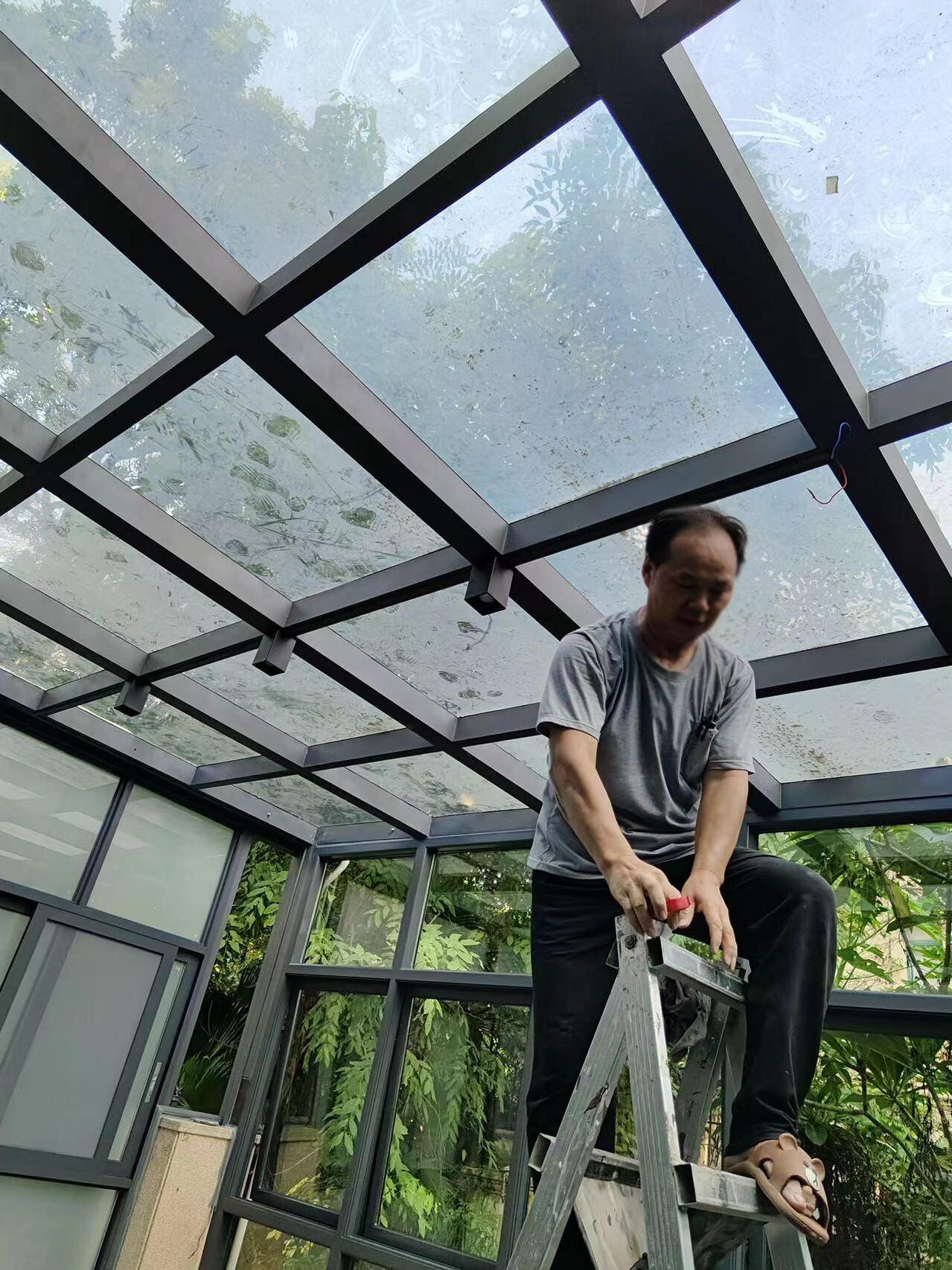 Square spots on black beams beneath a translucent glazed roof, with a person on a ladder