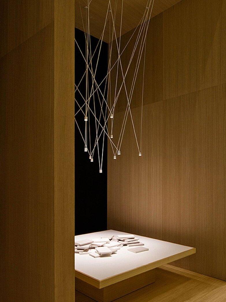White angular pendant arrangement in a wood-paneled display alcove above a floating table