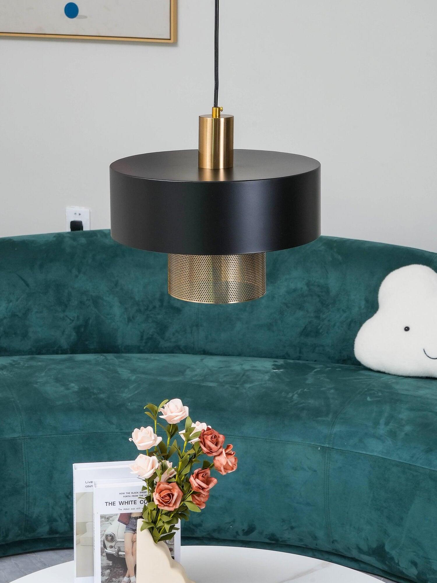 Closer Bradbury pendant view with black drum shade and copper-tone inner cylinder above flowers beside a teal sofa