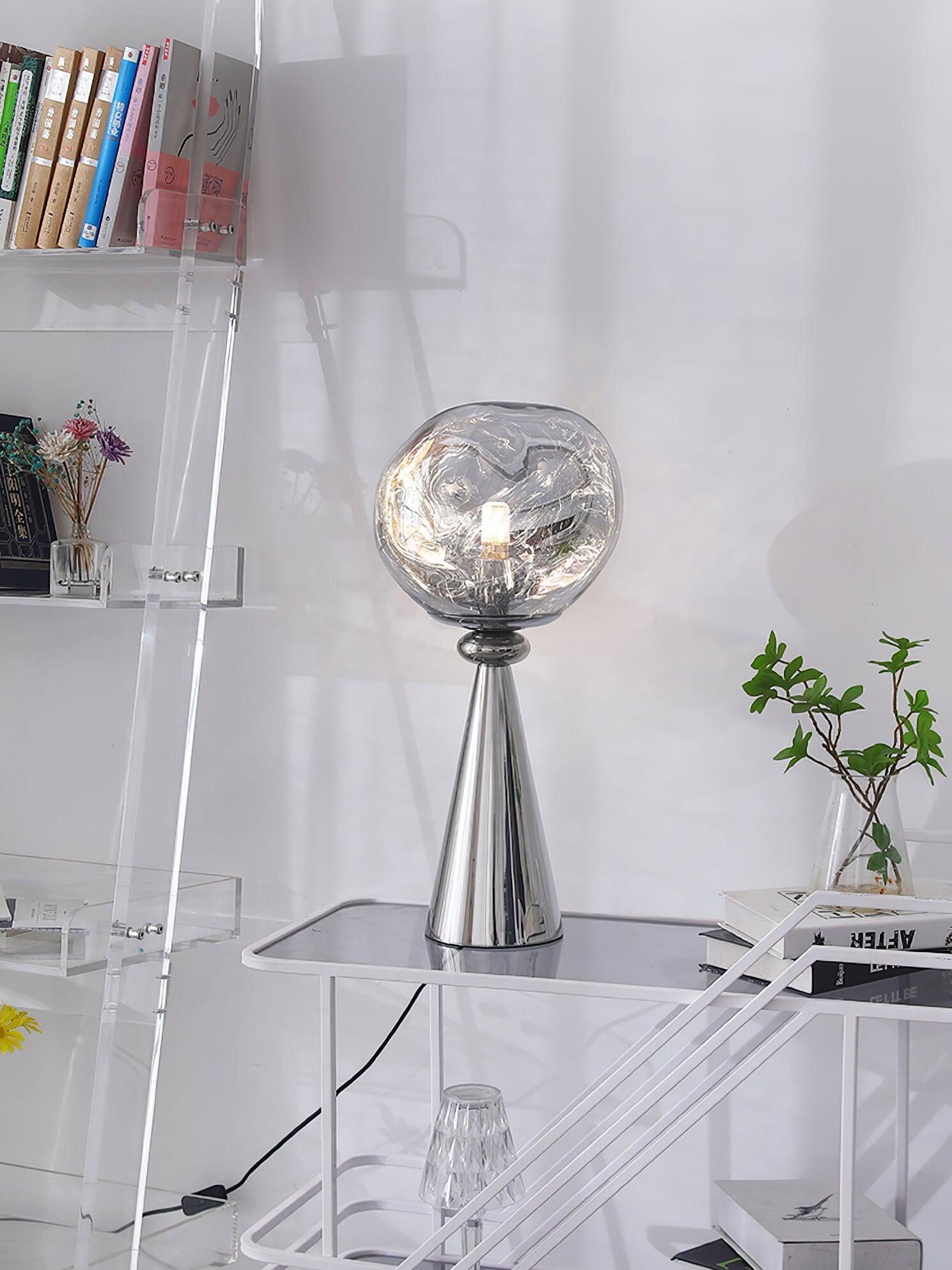 Chrome globe table lamp on a white cart beside a clear bookshelf, books and a plant, with a cord switch