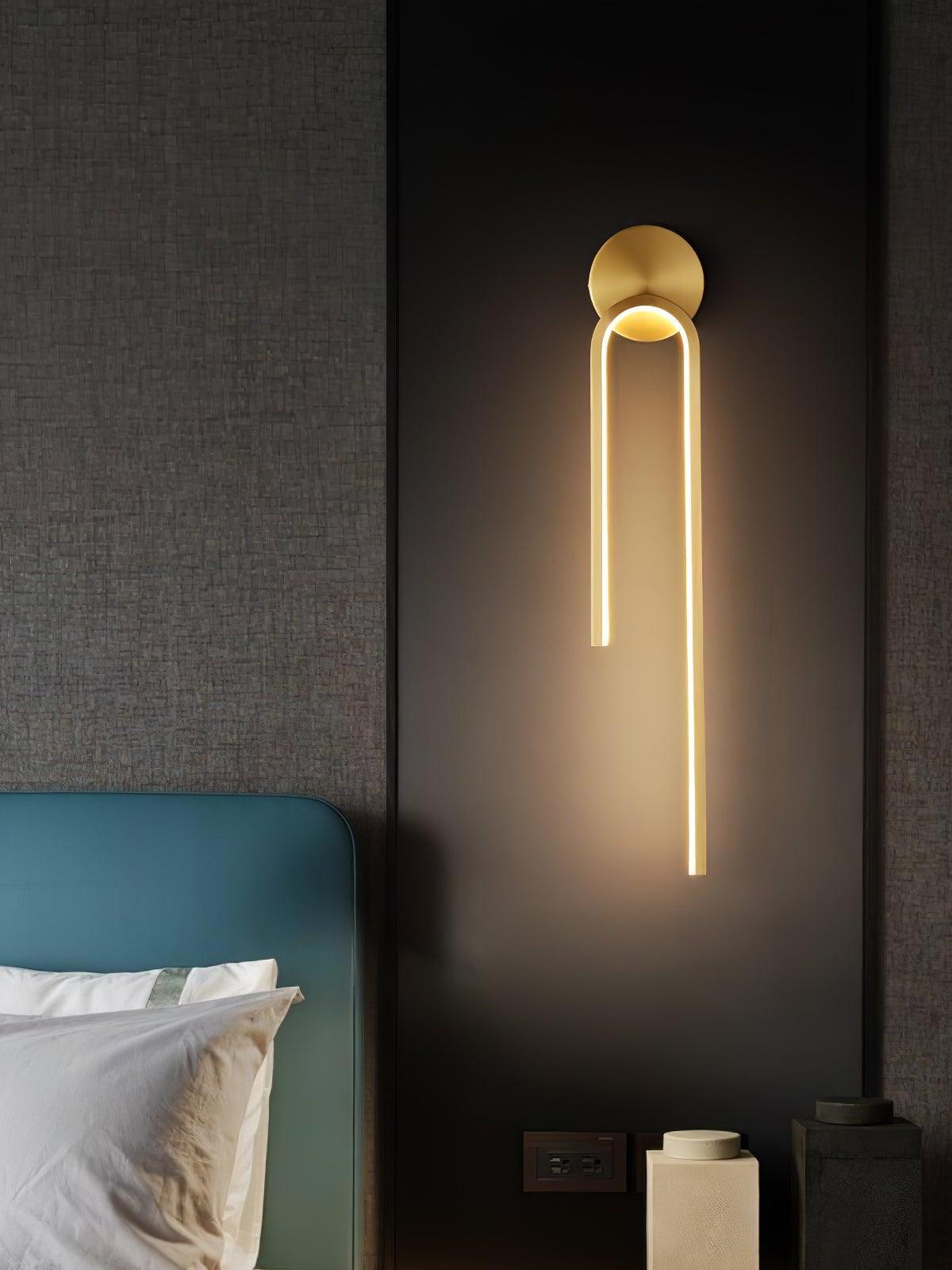 Gold-tone arch wall light with a long right arm beside a teal bedhead and dark wall panel