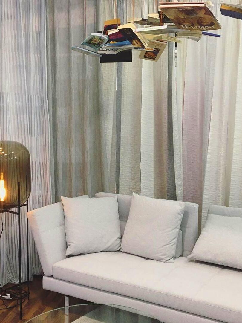 Tall glass lamp at the end of a white sofa beside sheer curtains.
