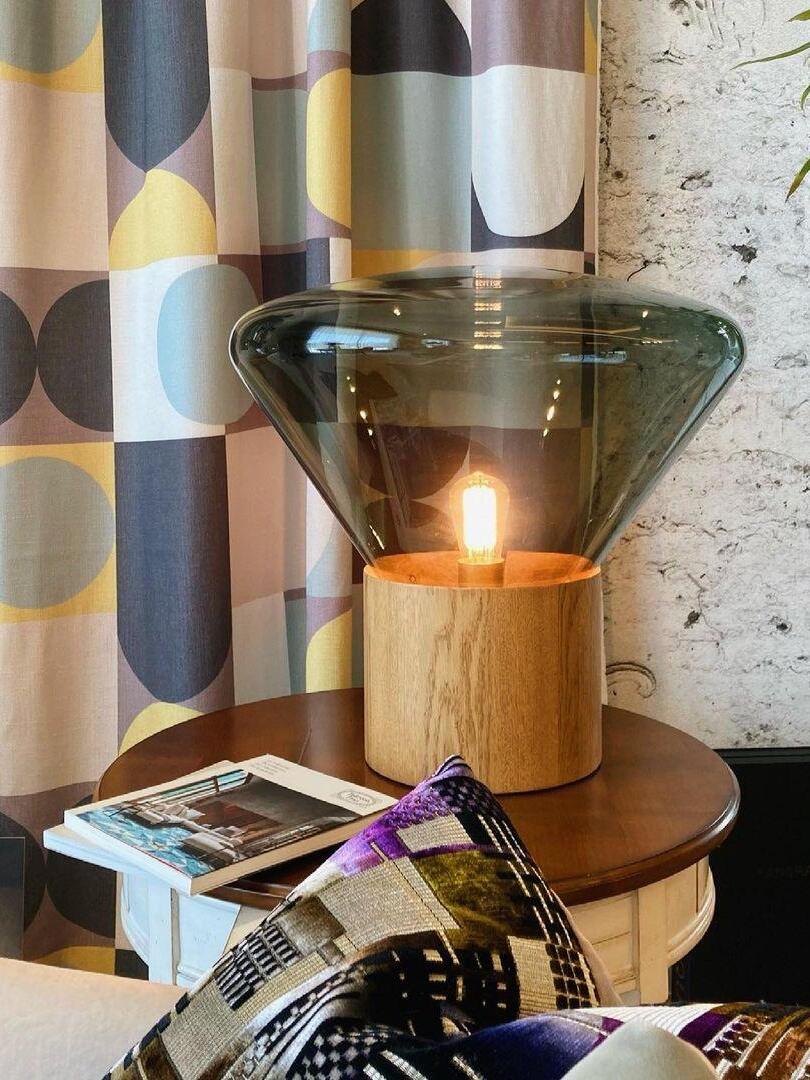 Lit smoky glass lamp on round side table beside patterned curtain and chair