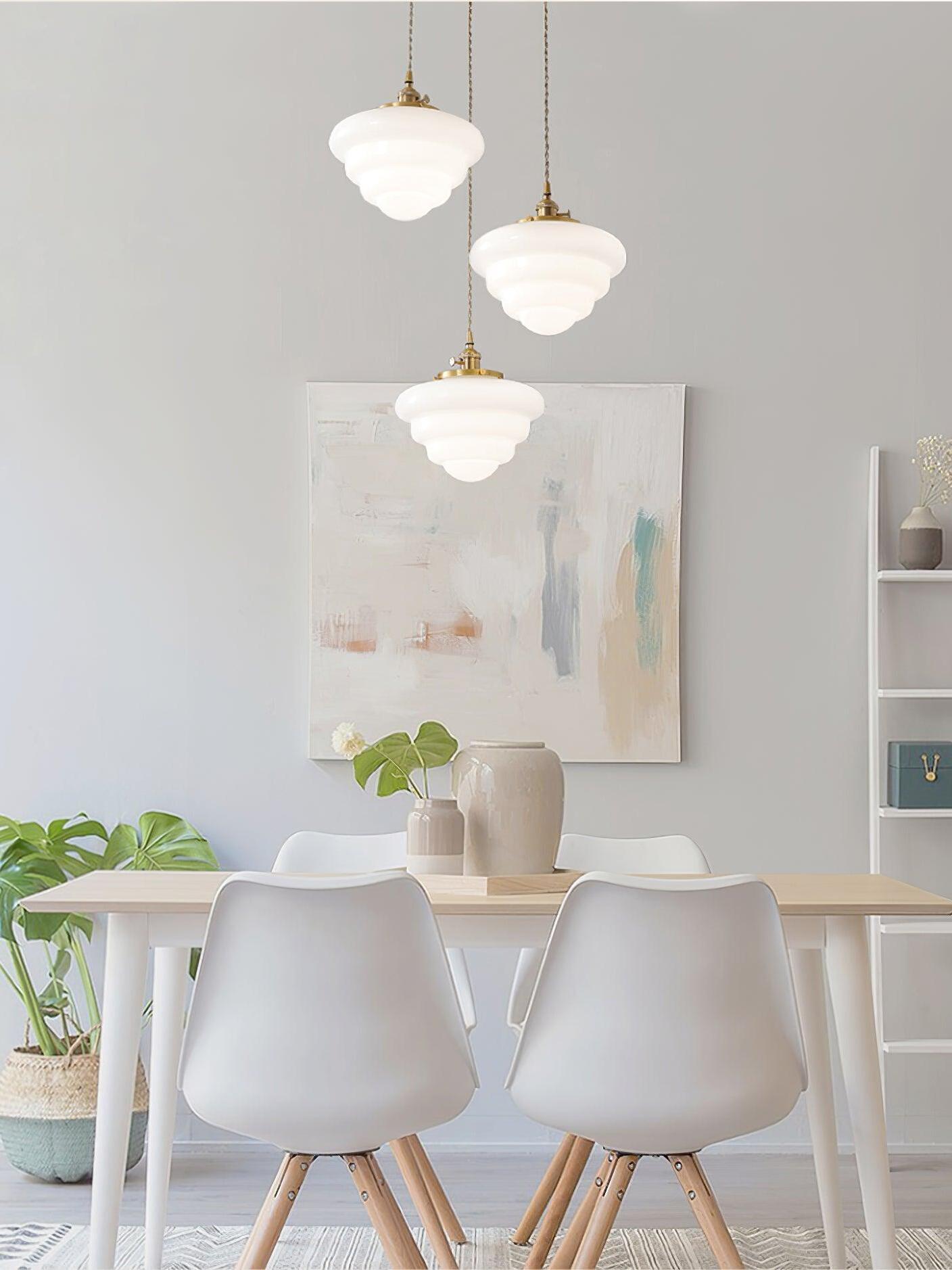 Three staggered Atlas Model B shades above a light wooden table and white chairs, with vases and an abstract painting