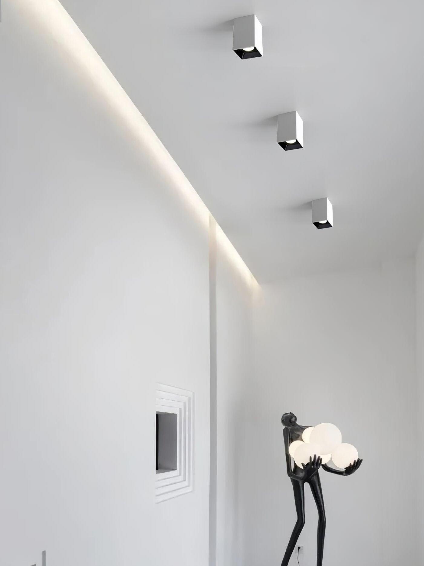 Three white ceiling spots beside a tall sculptural globe lamp against a white wall