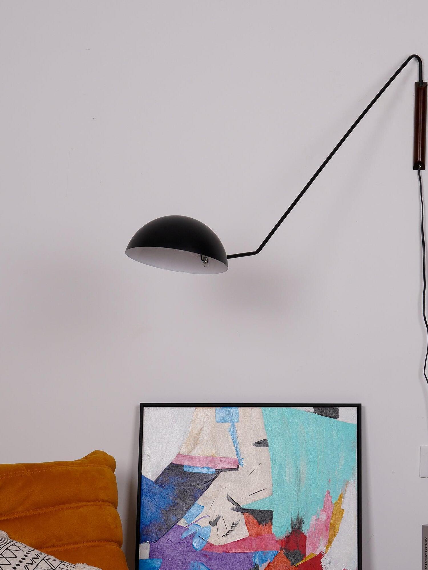 Closer view of black dome shade, white interior and long angular arm from a dark wooden wall mount above framed art