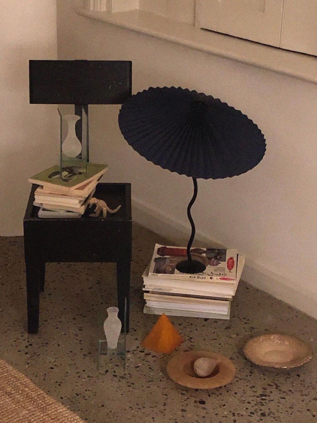 Black pleated-shade lamp on stacked books beside a rectangular-shade lamp and small decorative objects